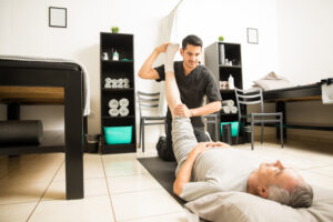 doctor assisting elderly patient with leg exercise in clinic